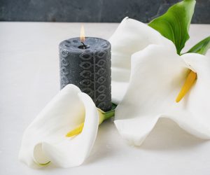 White Calla Lilly flowers with burning black candle on white background. Concept of mourning.